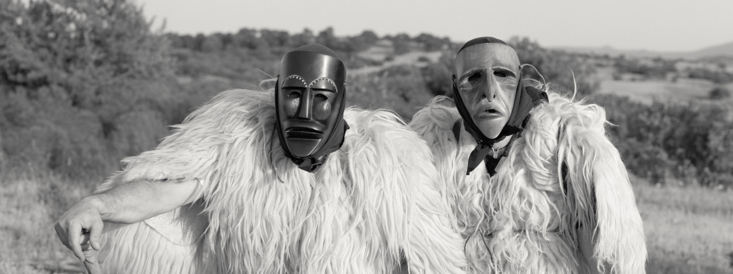 Two men in costume and with tribal masks on.