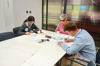 Three people seated around a table in a meeting room, reviewing documents and writing notes