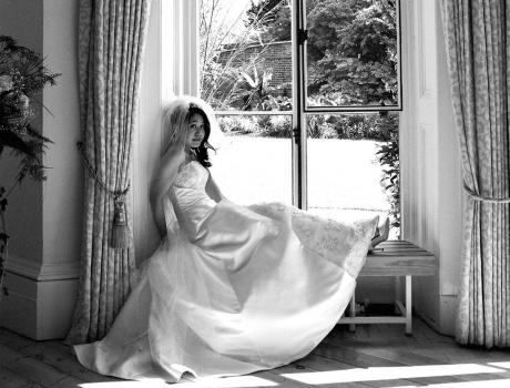 Black and white photo of lady in bridal dress posing in window