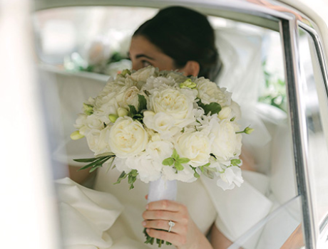 A bride sitting in the car with a white bouquet