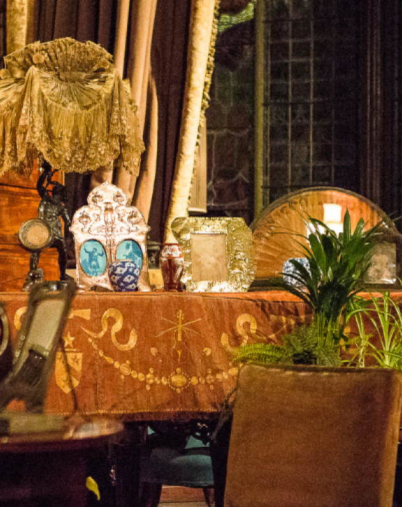 An actress dressed as a Victorian woman reading next to a piano in a room heavily decorated