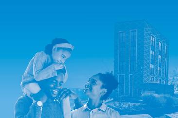 A family stands together outdoors with a child sitting on an adult’s shoulders