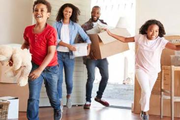 An excited young family run into the empty living room of their new home