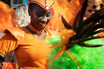 A black woman wearing a bright Orange samba costume dancing in the street during Notting Hill Carnival.