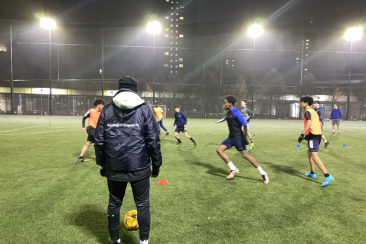 Football coach observes players training on a floodlit pitch at night