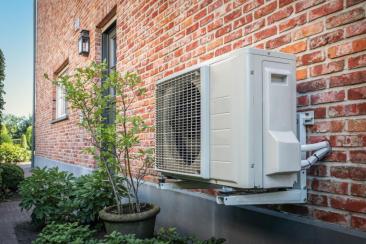 An outdoor heat pump unit mounted on the exterior wall of a brick house