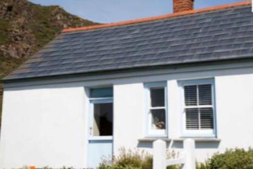 A small white house with a slate roof and Solar PV on a flat roof integrated with a green roof