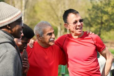 Group of residents taking part in an outdoor community activity, standing together with their arms around each other