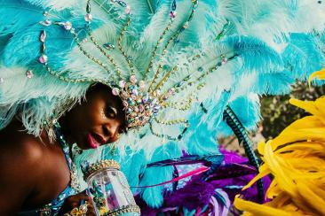 A woman dancing in the Notting Hill Carnival parade wearing a turquoise feather headdress.