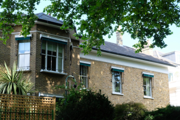 View of Phillimore gardens with sash windows and exterior window awnings, surrounded by mature garden plants and shaded by overhanging trees.