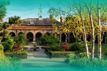 Historic brick building with an arched colonnade surrounding a landscaped courtyard, featuring paths, planting beds, water features and slender trees in the foreground