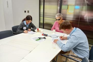 Group of three people sat around a table writing on paper