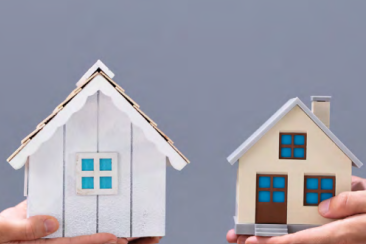 Two hands hold small model houses side by side against a plain background