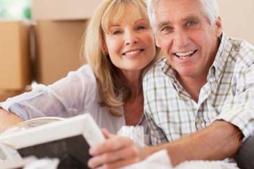 A man and woman are smiling as they unpack photos from one of the many cardboard boxes around them