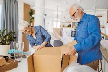 An older, grey-haired man and woman assemble a cardboard box on a kitchen table