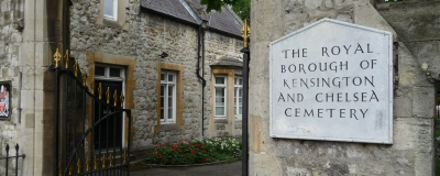 Stone walled entrance to Hanwell Cemetery with a sign on the wall reading ' The Royal Borough of Kensington and Chelsea Cemetery'