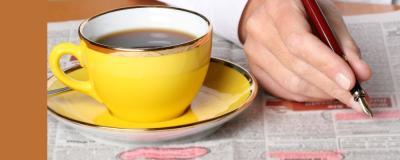 a yellow cup of coffee and someone circling text on a newspaper