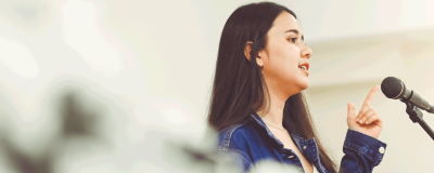 a woman talking in front of a microphone