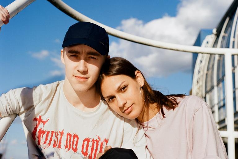 Two young people sit together, the young female rests her head on the males shoulder.