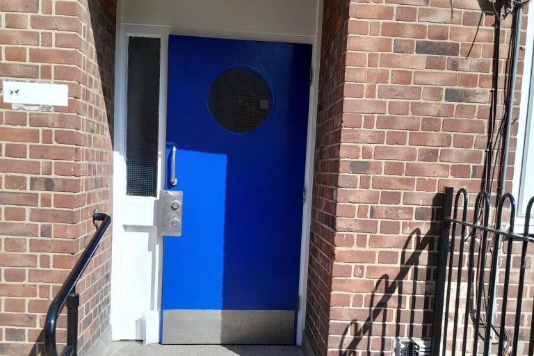 blue door with round window connected to red brick building with new silver fob entry