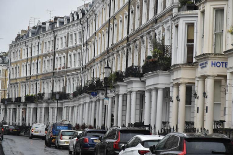 A street showing a row of tall terrace properties and parked cars