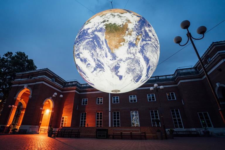 A large lit up Earth hangs over Jubilee Square which is lit with orange light