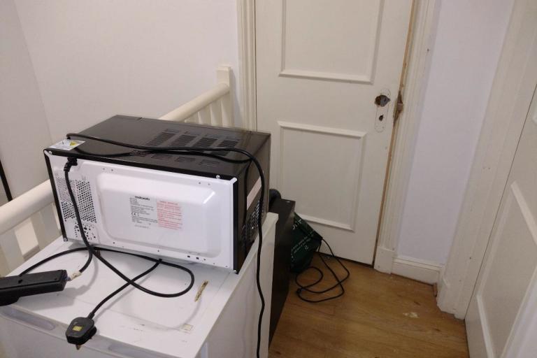 A fridge, microwave and vacuum cleaner block a communal means of escape, along with a damaged fire door.