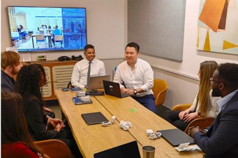 A group of people in a room with a display screen, having a discussion