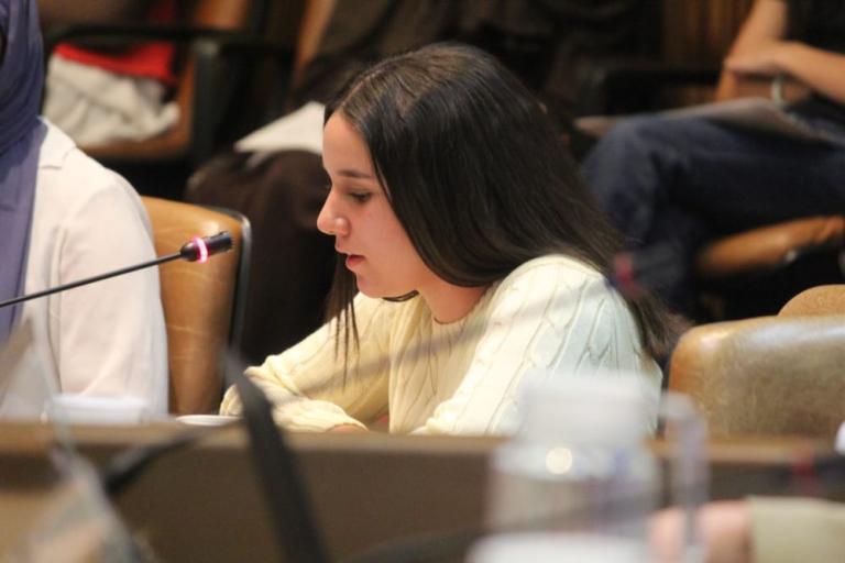 A young person sits at a microphone in the Council Chamber asking a question
