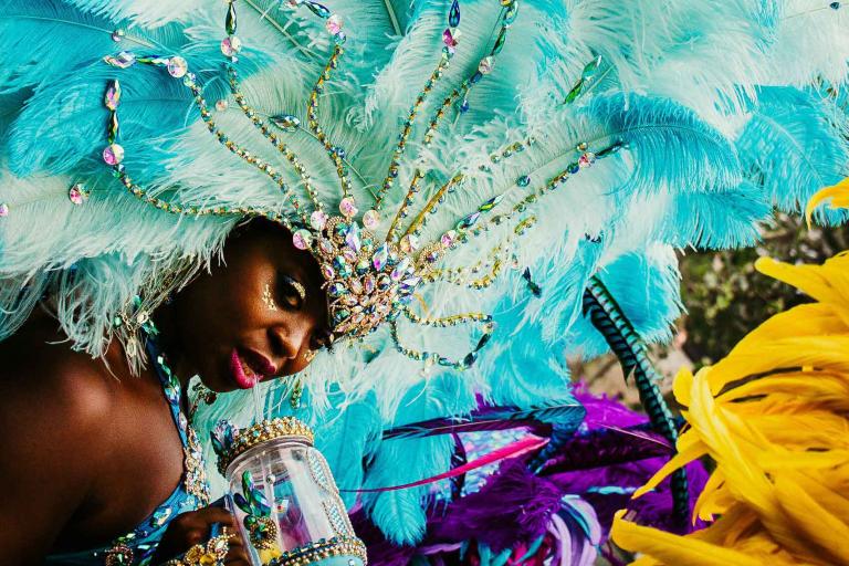 A woman dancing in the Notting Hill Carnival parade wearing a turquoise feather headdress.