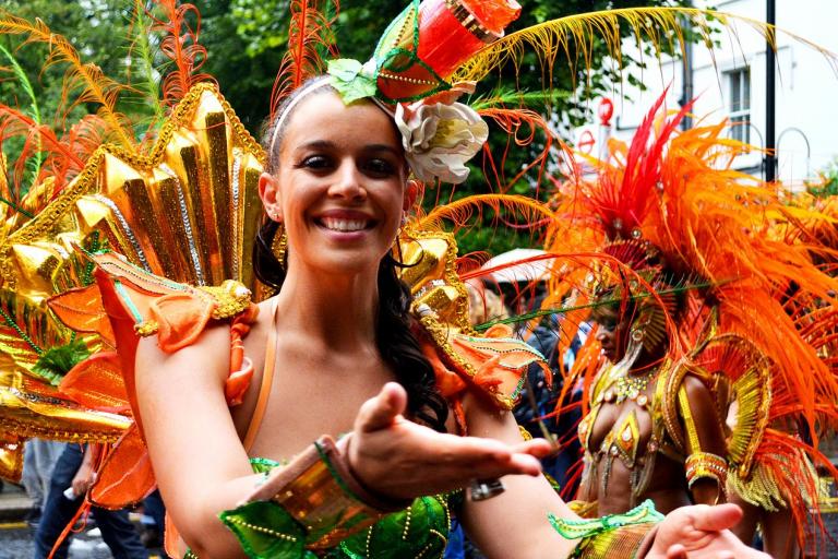 A women in brightly coloured costume smiles with hands outstretched to camera in welcoming signal