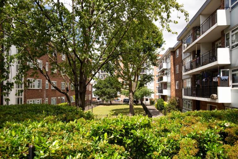 Image of housing buildings with balconies and trees in front with a big green garden