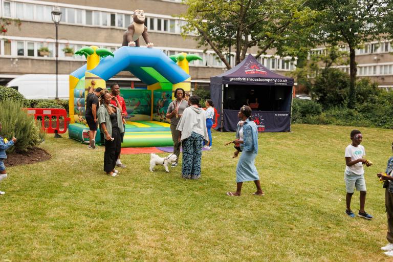 bouncy castlle in background and adults and children gathering on grass in foreground
