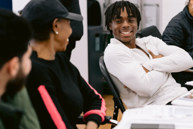 Young man folding his arms smiling and talking with others in a classroom