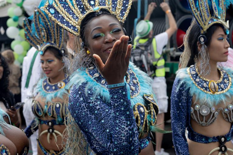 Female dressed in carnvial costume waving with two woman in the background also in carnival costume