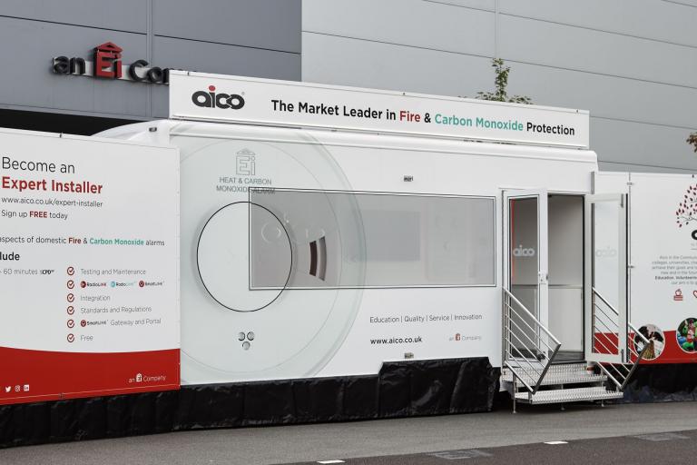 Image of a white trailer which has been converted into an office displaying the logos and signage of a company called Aico who specialise in smoke alarms and carbon monoxide detectors