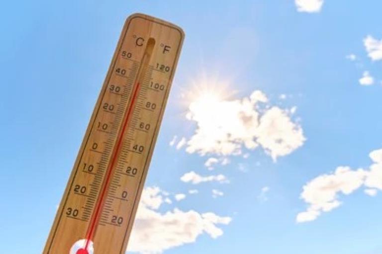 plastic thermometer held up infront of a blue sky with sunshine and few clouds 