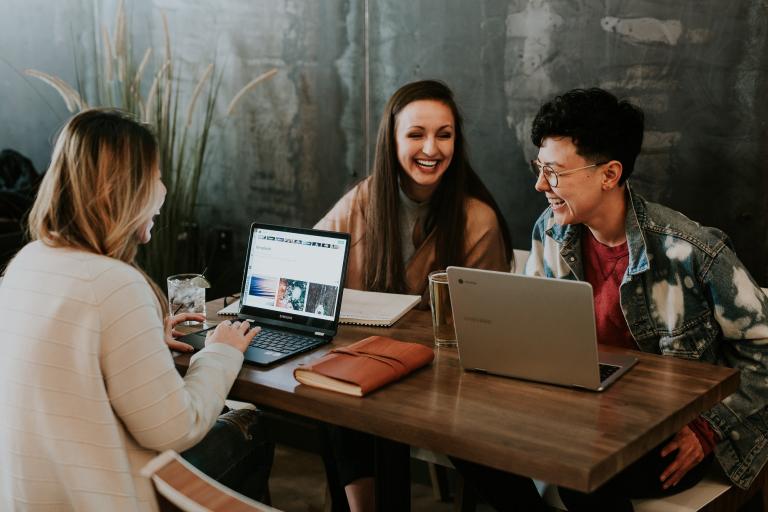 A group of young people working around a table on laptops