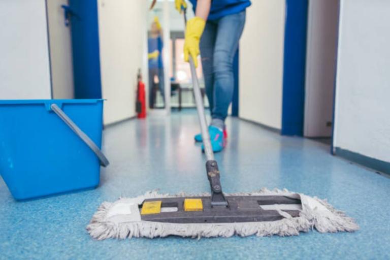 Man cleaning the floor of a corridor using a mop and wearing marigolds