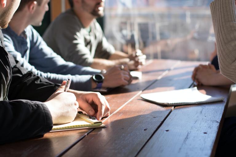 A group of people sitting at a table with notebooks and pens.