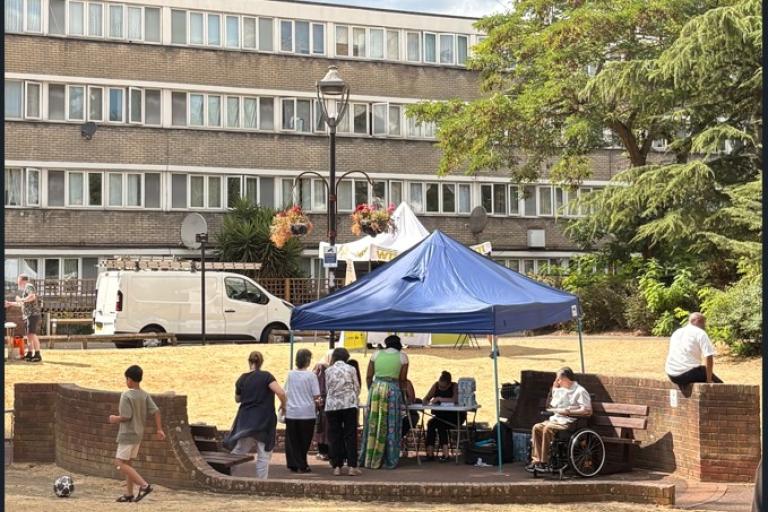 blue gazebo with six people standing underneath with low rise building in the background
