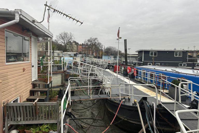 A walkway next to the River Thames with a blue houseboat in view on the water