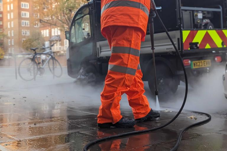 Worker jet washing a street with electric buggie in background