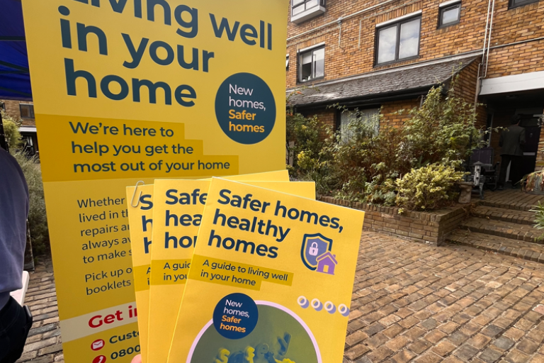 light green booklet being held up in front of a pull up banner saying living well in your home with a brick building in the background 