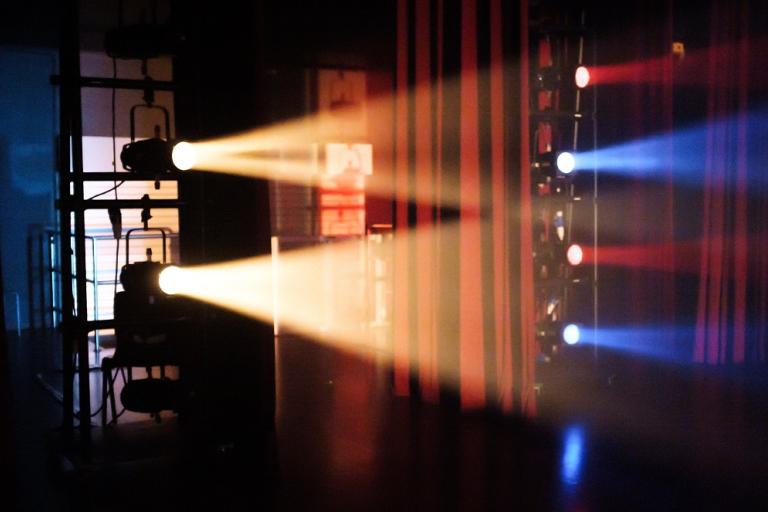 theatre lights emit a yellow light right across a red draped curtains while alternate red and blue lights also shine