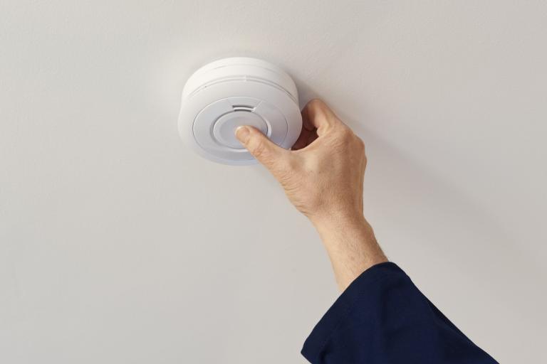 hand pressing centre button on smoke alarm