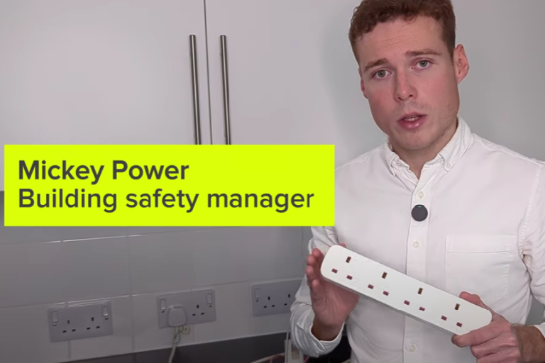 white male holding extension lead in front of white glossy kitchen 