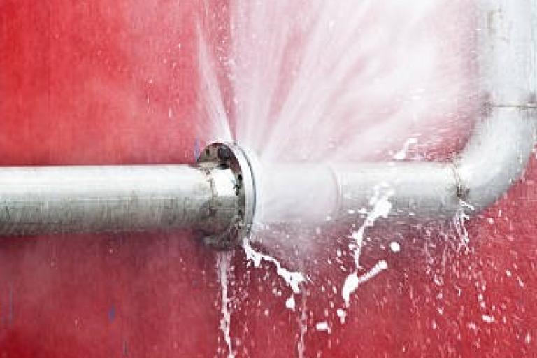 A burst pipe sprays water against a red wall