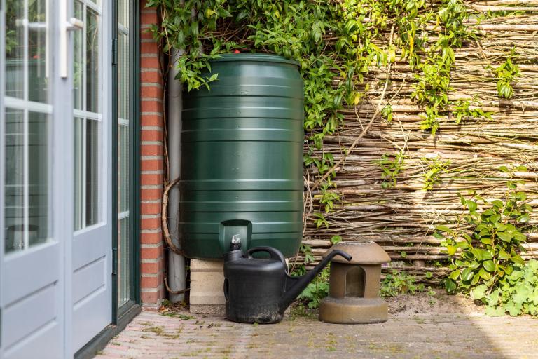 A patio with a green water butt and watering can