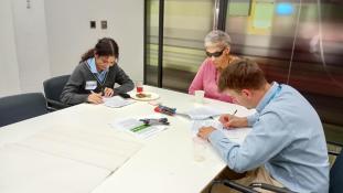 Group of three people sat around a table writing on paper